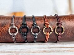 four different bracelets are sitting on a leather wrap around each other, one with an oval clasp and the other with a loop