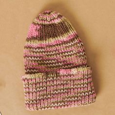 a pink and brown knitted beanie sitting on top of a cardboard box next to a pair of scissors