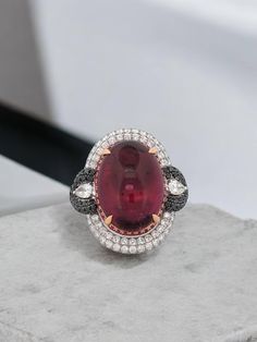 a ring with a large red stone surrounded by white and black diamonds on a rock