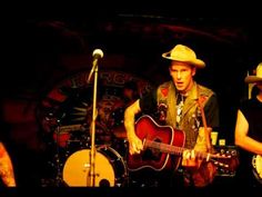 two men are playing guitars and singing into microphones while another man stands behind them