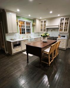 a large kitchen with white cabinets and wooden table in it's center island surrounded by chairs