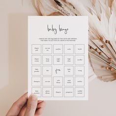 a person holding up a baby shower game on top of a white table next to feathers