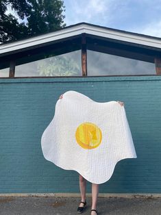 a woman holding up a towel with an egg on it in front of a building