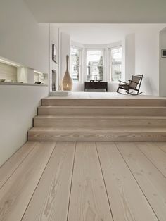 a room with white walls and wooden floors has a rocking chair on the stairs next to it