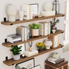 three wooden shelves with books, plants and pictures on them in the corner of a room