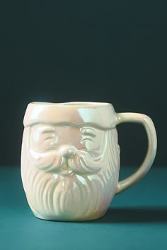 a white ceramic mug with a beard and mustache on the handle is sitting on a green surface