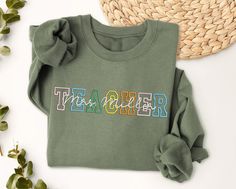 a t - shirt with the word teacher on it sitting next to some plants and a straw hat