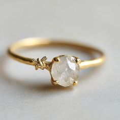 a gold ring with a white diamond in the middle and a tiny bee on it