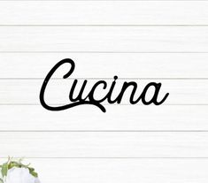 the word cucina written in black ink on a white wooden background with flowers and greenery