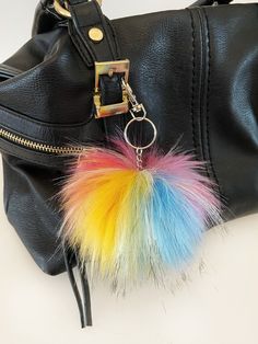 a black purse with a multi colored pom - pom keychain hanging from it