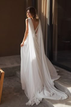 a woman in a white dress is standing near a couch and looking out the window