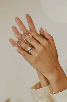 a woman's hands with white manicured nails and a ring on her left hand