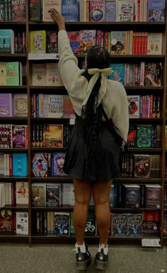 a woman standing in front of a bookshelf with her hand up to the sky