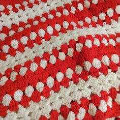 a red and white crocheted blanket is laying on the floor