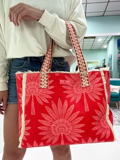 a woman holding a red bag with white flowers on the front and side, in an airport