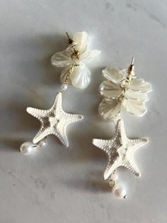 White Flower and Pearl Knobby Starfish Handmade Earrings. Introducing an exclusive LIVE COASTAL design!  Elevate your vacation style with these beautiful, handmade pearl and starfish earrings - a one-of-a-kind accessory that effortlessly complements any stunning ensemble! These hanging pearl earrings are made of faux pearl flowers, hanging pearl and high quality alloy with gold detailing. I've added the perfect little mini knobby starfish on one of the pearls for a beachy touch.  They are lightweight, hypoallergenic and nickel-free, easy to wear and measure approximately 3.5" long. The earrings arrive in a small gift box. They hang beautifully on the ear as seen on the model in the pictures. These earrings are eye-catching and create a truly dramatic and beach inspired look! Perfect for be Coastal Accessories, Accessories Beach, Flowers Hanging, Pearl Flowers, Starfish Earrings, Small Gift Boxes, Coastal Design, Beach Weddings, Themed Jewelry