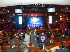 an auditorium full of people sitting and standing in front of large screen television's