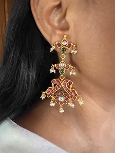 These stunning Kempu 925 silver earrings are meticulously handcrafted by fine jewelry artisans, featuring an elegant peacock design with natural freshwater pearl drops. Perfect for destination weddings and festive seasons like Navratras, these earrings combine traditional charm with intricate detailing, making them an ideal accessory for special occasions. Weight: 36 grams per pair Materials: 925 Silver, Kempu Stones, Freshwater Pearls, Gold Plated. Closure Type: Push Back Closure. Dimensions: Length is 7.5 cm and width is 4 cm. Designed to enhance your festive look, these earrings offer a perfect blend of comfort and sophistication. Festive Silver Pearl Earrings With Elegant Design, Traditional Pearl Drop Earrings In Sterling Silver, Festive Sterling Silver Pearl Drop Earrings, Elegant Sterling Silver Bridal Earrings For Festive Season, Elegant Sterling Silver Bridal Earrings, Elegant Festive Sterling Silver Bridal Earrings, Elegant Sterling Silver Pearl Earrings For Festive Occasions, Elegant Sterling Silver Earrings With Peacock Design, Elegant Silver Danglers With Peacock Design