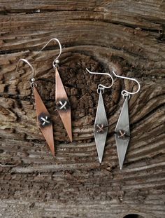 three pieces of metal sitting on top of a piece of wooden plank with silver earwires