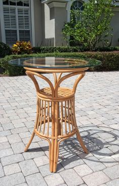 a round table with glass top sitting on a brick walkway in front of a house