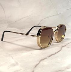 These aviator sunglasses feature a vintage 70s-inspired design with an octagonal shape. The lenses have a stylish brown ombre tint, perfectly complemented by a sleek gold metal frame. Suitable for both men and women, these shades add a retro flair to any look while offering classic pilot style. NOS Deadstock Made in Europe FIT INFORMATION  55mm Eye Size 22mm Bridge 145mm Temple/Arm Width 5 Inches Height 1 3/4 Inches Luxury Elegant Men's Aviator Sunglasses, Tan Luxury Sunglasses, Luxury Gold Aviator Sunglasses With Metal Frame, Luxury Vintage Gold Aviator Sunglasses, Retro Aviator Sunglasses With Metal Frame, Retro Aviator Sunglasses With Uv Protection And Square Frame, Retro Square Frame Aviator Sunglasses With Uv Protection, Retro Metal Frame Sunglasses, Retro Brown Shield Sunglasses With Square Frame