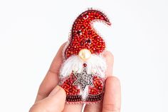 a hand holding a red and white beaded santa clause ornament with a star on it