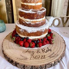 a three tiered cake with strawberries and blueberries on the bottom is displayed on a wood slice