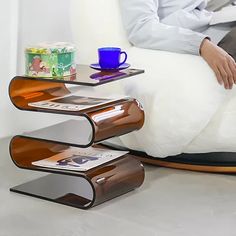 a man sitting in a chair with a coffee cup on top of the table and magazine rack