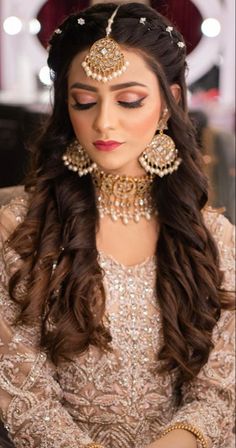 a woman with long hair and jewelry on her head sitting in front of a mirror