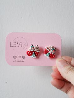 someone is holding up a pair of christmas themed earrings on a pink card that says levi