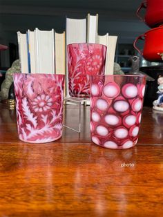 four glass cups sitting on top of a wooden table next to an open bookcase