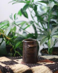 a brown vase sitting on top of a table next to a potted green plant