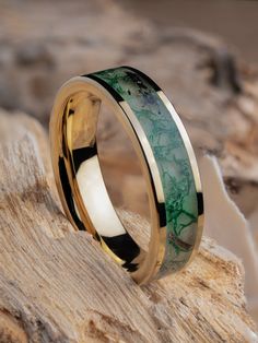 a wedding band with green and black marble inlays on top of a rock