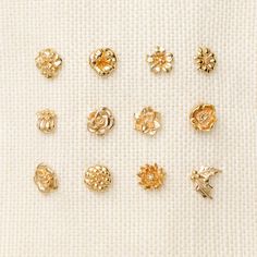 six pairs of gold - plated flower studs on a white cloth, each with four different designs