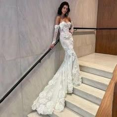 a woman in a white wedding dress standing on some stairs with her hand on the rail