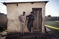 two men standing in front of a building with an open door and one leaning against the wall