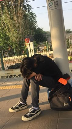 a man sitting on the ground with his head in his hand next to a bag