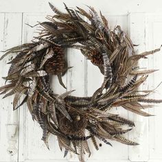 a wreath made out of dried plants and pine cones hanging on a white wooden door