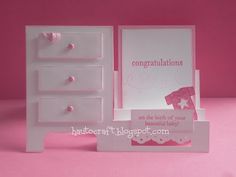 a white dresser with two drawers and a card holder on it's side, against a pink background