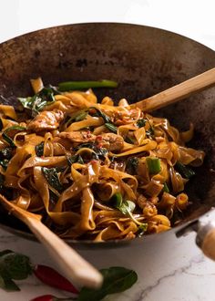 a wok filled with noodles and vegetables on top of a marble counter next to wooden utensils