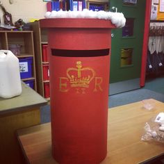 a red trash can sitting on top of a wooden table next to a book shelf