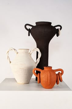 three different vases sitting on top of a white shelf next to each other in front of a white wall