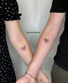 two people holding hands with small tattoos on their arms, one has a heart and the other has a cross