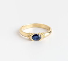 a yellow gold ring with a blue sapphire and two diamonds on the side, sitting on a white surface