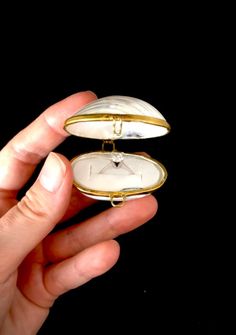 a person is holding two small pieces of jewelry in one hand and an open pocket watch in the other