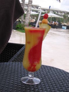 a colorful drink sitting on top of a table next to an umbrella and beach in the background