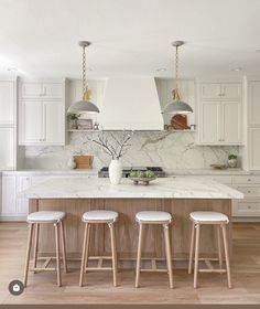 a kitchen with marble counter tops and stools in front of an island that has three lights hanging from it