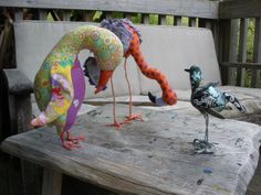 two birds sitting on top of a wooden table next to each other near a bench