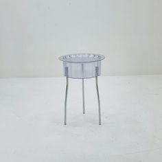 a clear glass table with metal legs on a white floor in front of a wall