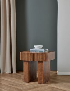 a table with a bowl on top of it in front of a curtained window